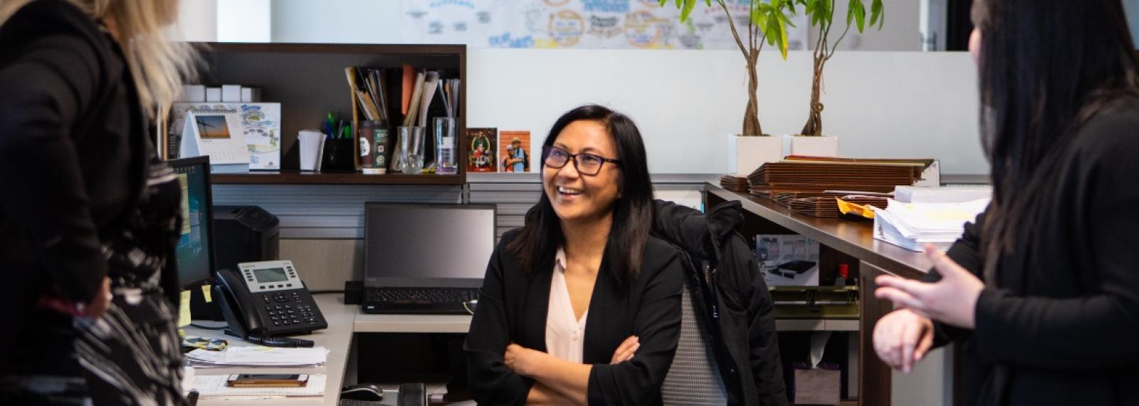 A woman sitting at her desk talking to co-workers